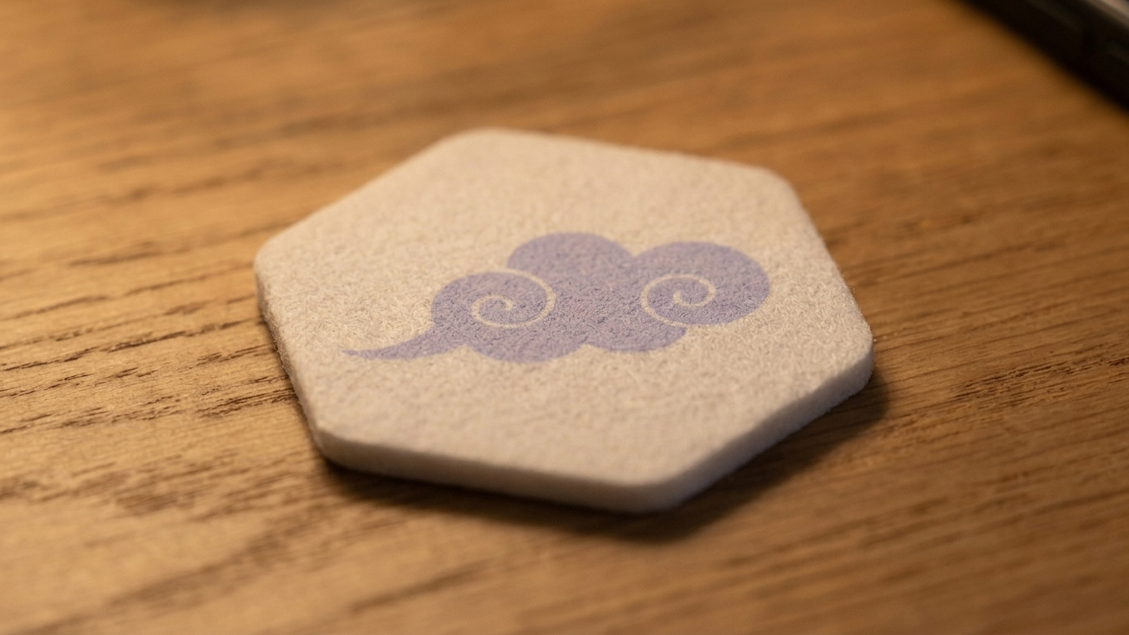 A white hexagonal felt patch with a pale purple cloud mark on its front surface.