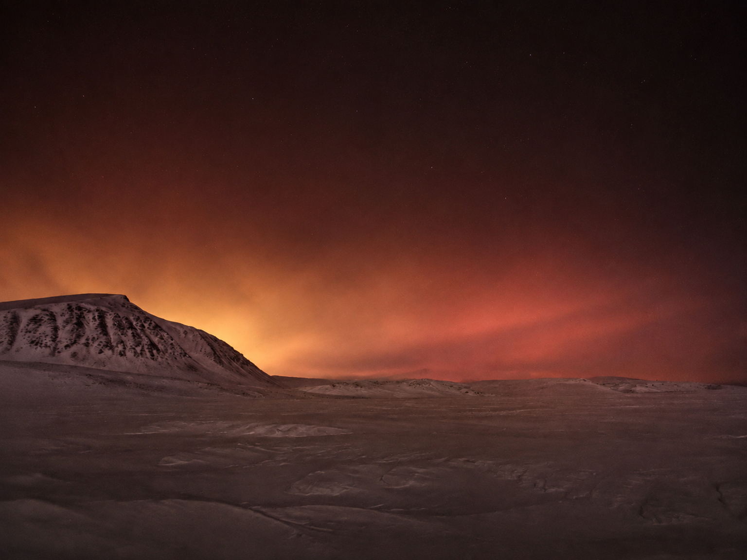 Snowfield and ridge beneath a faint aurora at night.